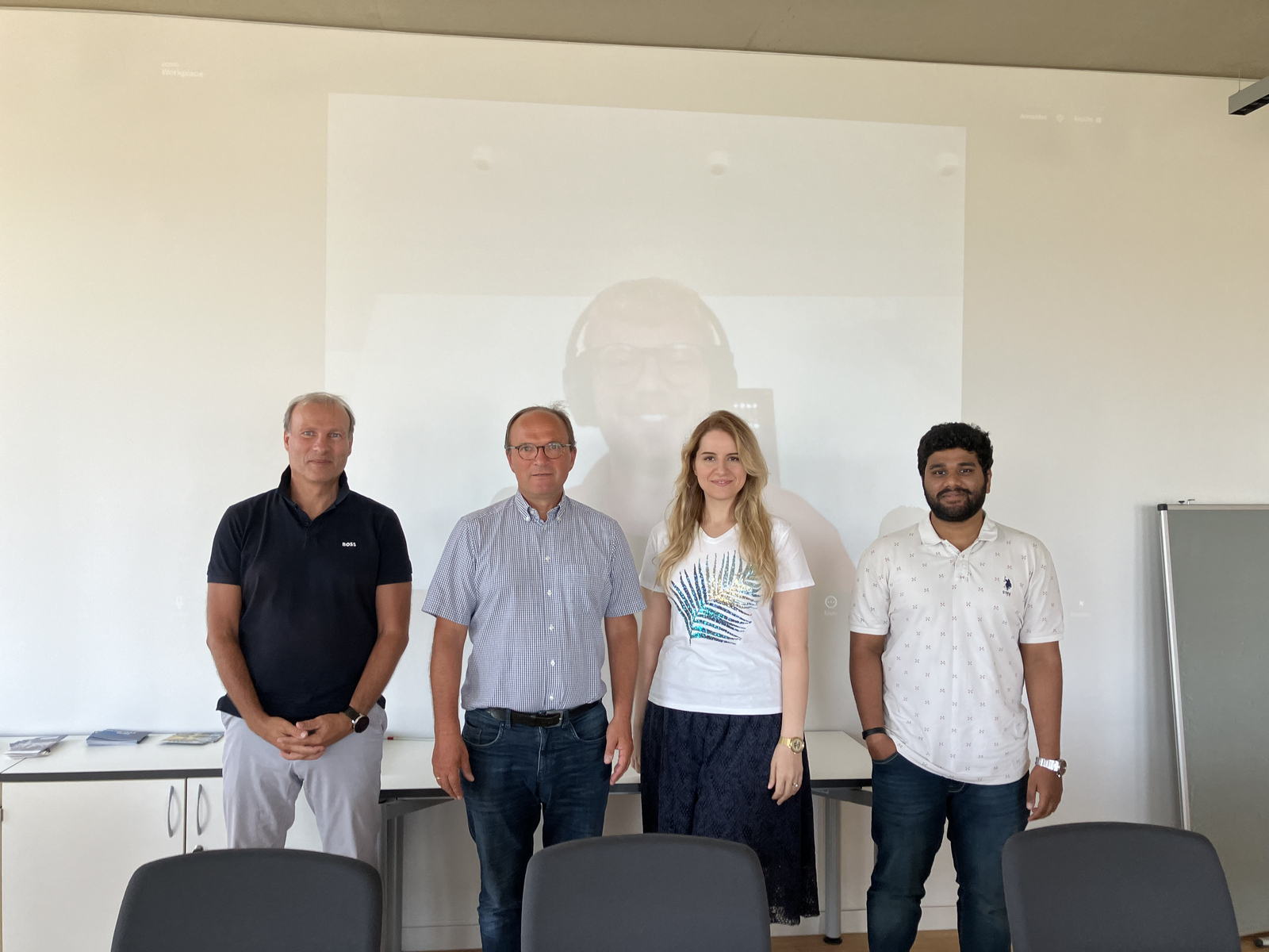 4 Personen vor einer Leinwand auf der der 5. Teilnehmer zu sehen ist