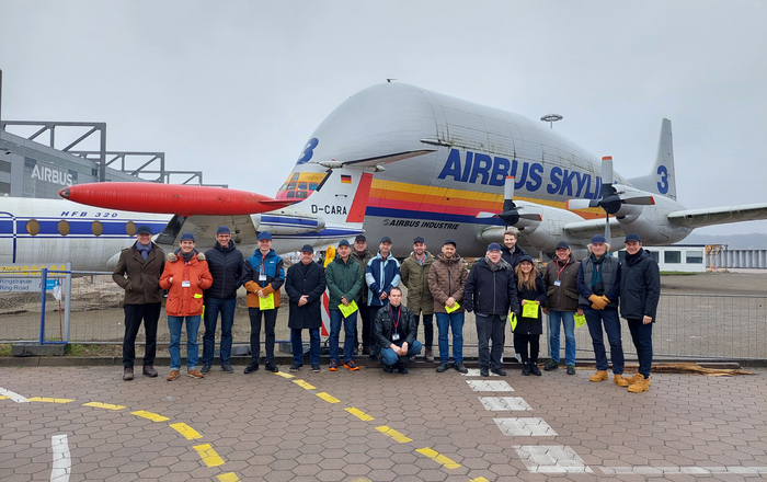 Die Projektbeteiligten stehen auf dem Firmengelände vor einem Airbus