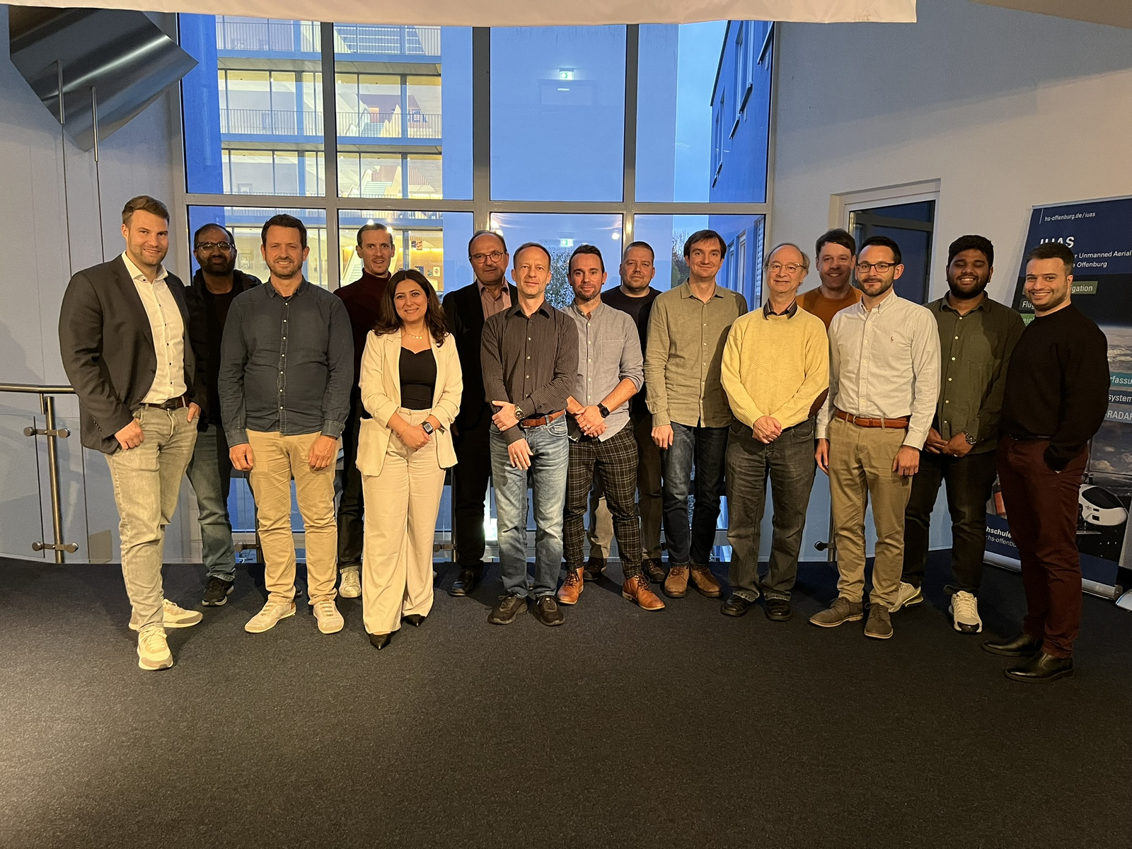 15 Personen stehen als Gruppe nebeneinander ein einer Reihe