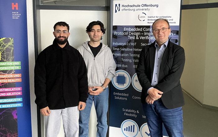 3 Personen neben einem RollUp des Insitutes