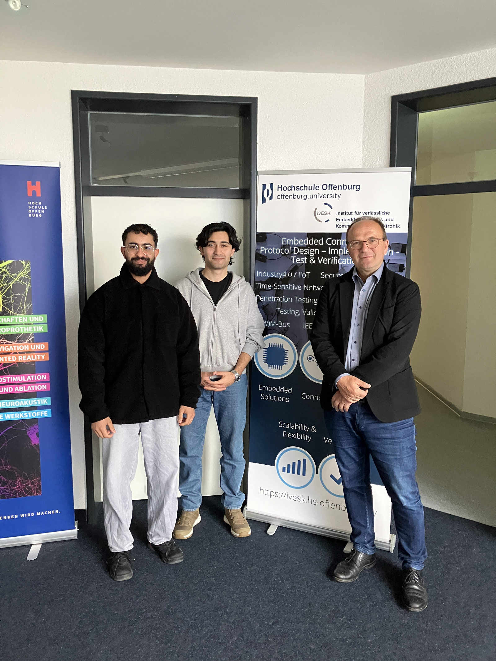 3 Personen neben einem RollUp des Insitutes